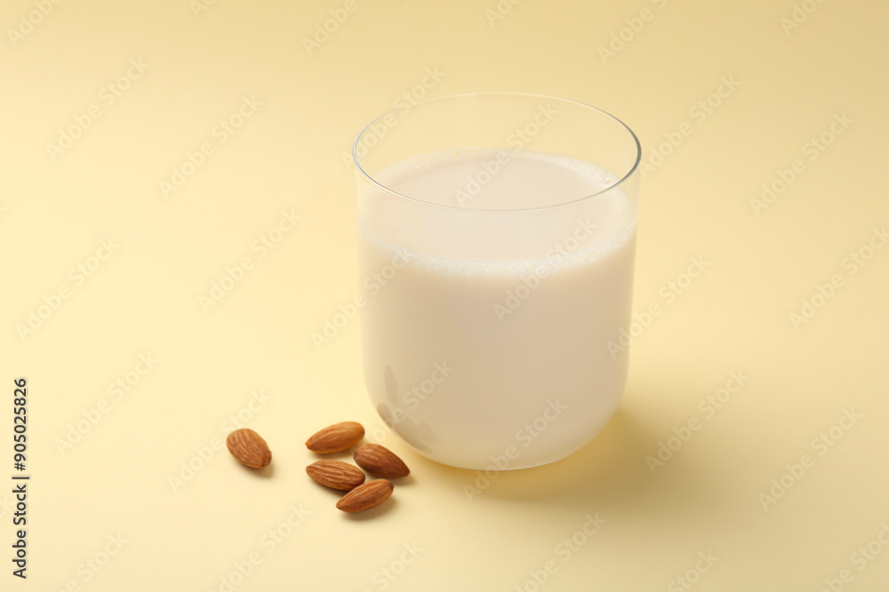 Fresh almond milk in glass and nuts on beige background Fresh almond milk in glass and nuts on beige background