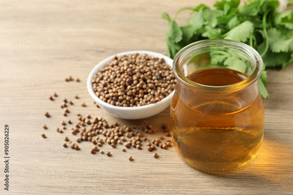 Dried coriander seeds in bowl, oil and green leaves on wooden table Dried coriander seeds in bowl, oil and green leaves on wooden table