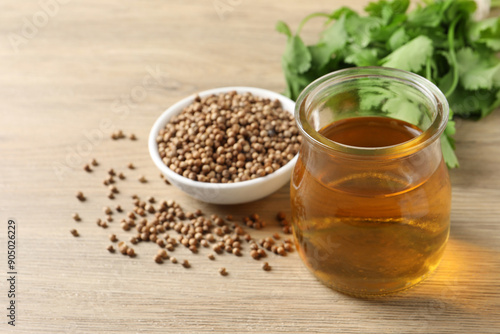 Dried coriander seeds in bowl, oil and green leaves on wooden table