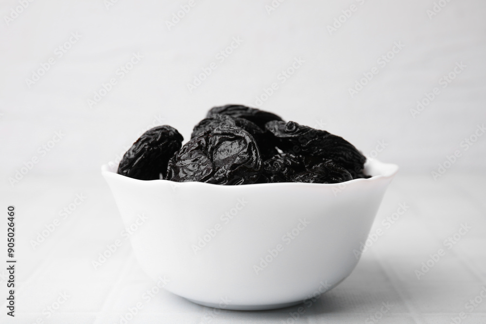 Tasty dried plums (prunes) in bowl on white tiled table, closeup Tasty dried plums (prunes) in bowl on white tiled table, closeup