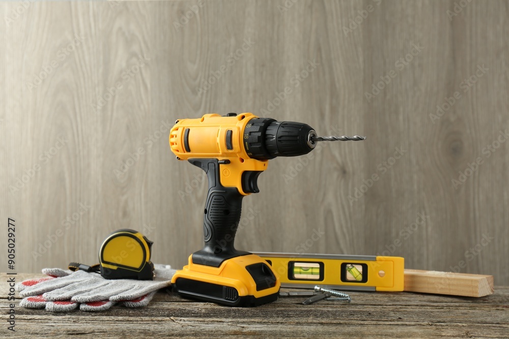 Cordless electric drill, gloves, bits, measuring tape and building level on wooden table Cordless electric drill, gloves, bits, measuring tape and building level on wooden table