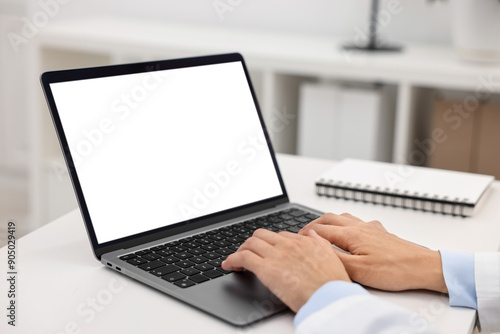 Doctor using laptop at white table in hospital, closeup