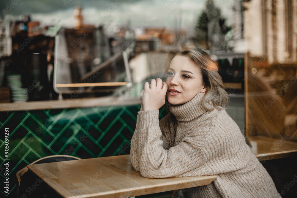 A woman is sitting at a table in a cafe, wearing a sweater and looking at the camera A woman is sitting at a table in a cafe, wearing a sweater and looking at the camera