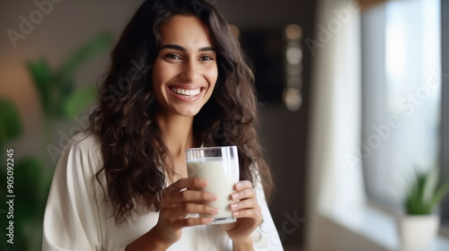 Health care, pretty young indian woman, girl drinking a glass of white fresh, dairy milk for calcium, vitamin wholesome good nutrition in morning at kitchen