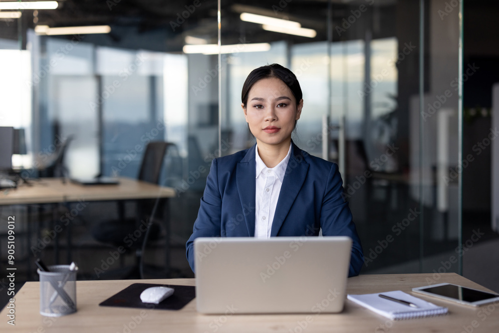 Confident businesswoman in blue suit using laptop at modern office desk. Professional work environment with natural daylight from large windows. Concept of leadership, corporate culture, technology. Confident businesswoman in blue suit using laptop at modern office desk. Professional work environment with natural daylight from large windows. Concept of leadership, corporate culture, technology.