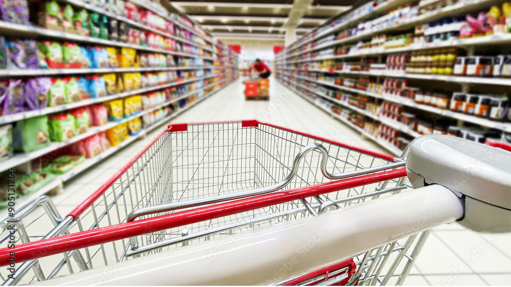 Fototapeta premium Pusty koszyk, wózek sklepowy w supermarkecie, rozmazane tło, wnętrze sklepu, supermarketu, wózek na zakupy, półki sklepowe z produktami. Hipermarket. Miejsce na tekst.