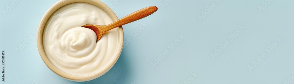 Creamy yogurt in a bowl with a wooden spoon against a light blue background, perfect for culinary and health-related visuals. Creamy yogurt in a bowl with a wooden spoon against a light blue background, perfect for culinary and health-related visuals.