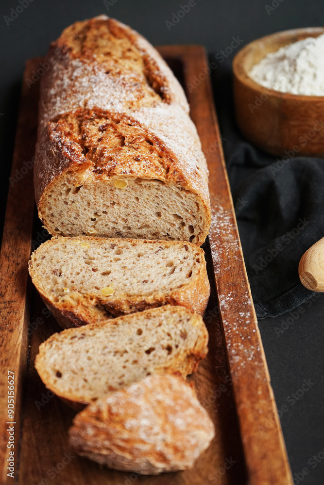 Fresh sliced bread on a wooden tray next to a bowl of flour and a wooden rolling pin on a dark background Fresh sliced bread on a wooden tray next to a bowl of flour and a wooden rolling pin on a dark background