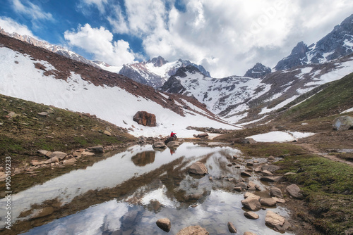 A small figure of a girl is reflected in the water of a glacial lake against the backdrop of snow-capped mountains and a blue sky. photo