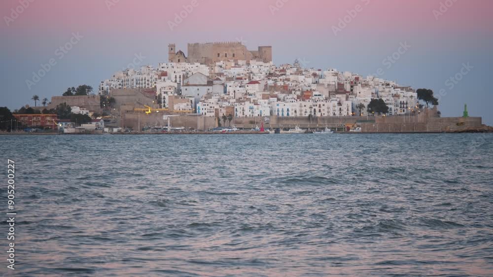 Slow tilt up reveal of the city of peniscola at sunset as the waves crash against the rocks in slowmotion zoomed in Slow tilt up reveal of the city of peniscola at sunset as the waves crash against the rocks in slowmotion zoomed in