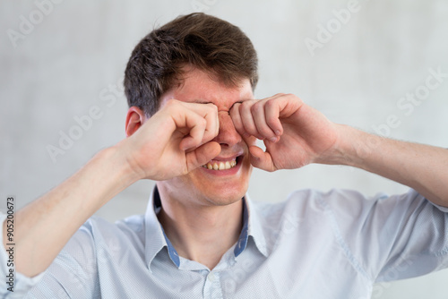 Man scretching itchy eyes on gray background photo