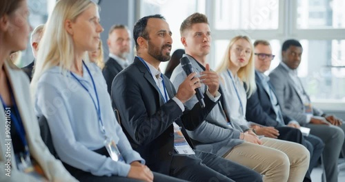 Multiethnic Male Technology Conference Attendee Sittign In Crowd And Using Microphone To Ask A Question Related To Presentation Of An Innovative Gadget. Middle Eastern Man At International Tech Forum. photo