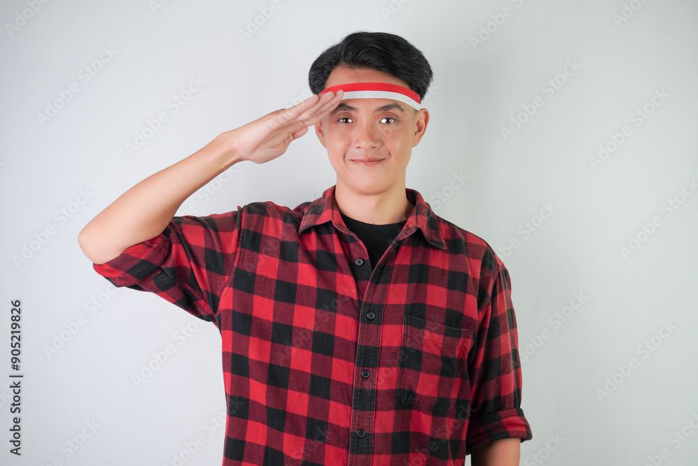 Excited young asian man wearing Indonesian flag headband, smiling expression with saluting gesture, isolated over white background. Concept for Indonesian Independence Day. Excited young asian man wearing Indonesian flag headband, smiling expression with saluting gesture, isolated over white background. Concept for Indonesian Independence Day.