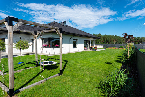 Beautiful garden with green grass, visible terrace table and house in beautiful summer weather, very wide shot.