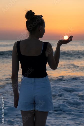 girl or woman on the beach towards a beautirful sunset holding the sun photo