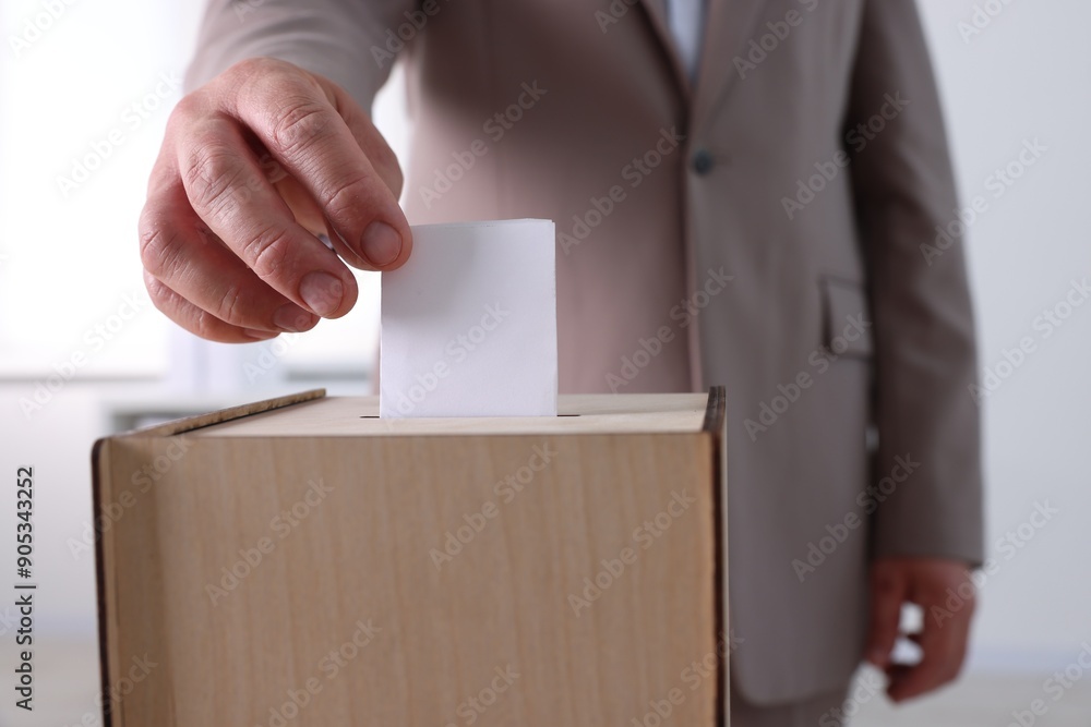 Man putting his vote into ballot box indoors, closeup
