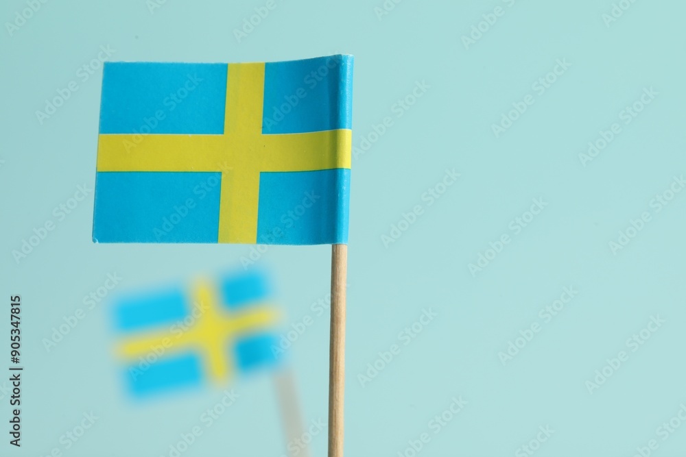 Obraz premium Small paper flags of Sweden on light blue background, selective focus. Space for text