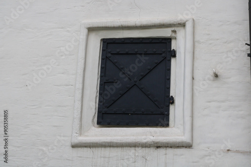 A small window covered with a black metal shutter with a lock in an old house