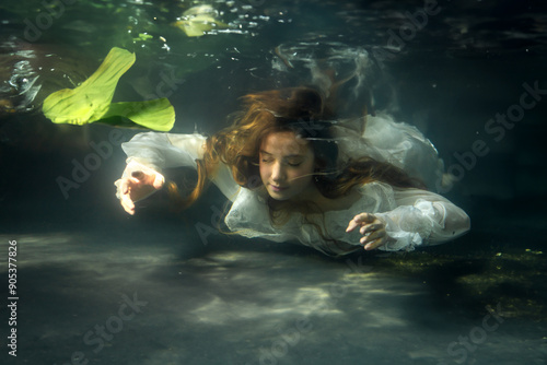 Beautiful blonde long haired girl in white dress posing in pond with green plants. Fairytale story about ophelia .Warm art work photo