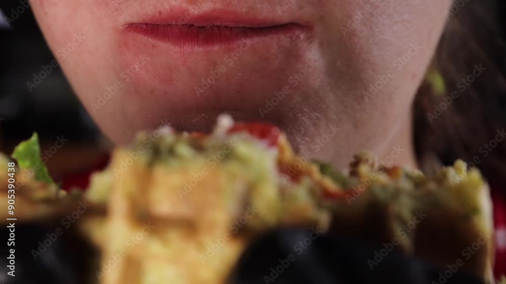 A woman eats a waffle burger with fresh lettuce, salad tomatoes, and cheddar cheese. Close-up of her biting into the waffle burger. Fast food.
A woman eats a waffle burger with fresh lettuce, salad tomatoes, and cheddar cheese. Close-up of her biting into the waffle burger. Fast food.