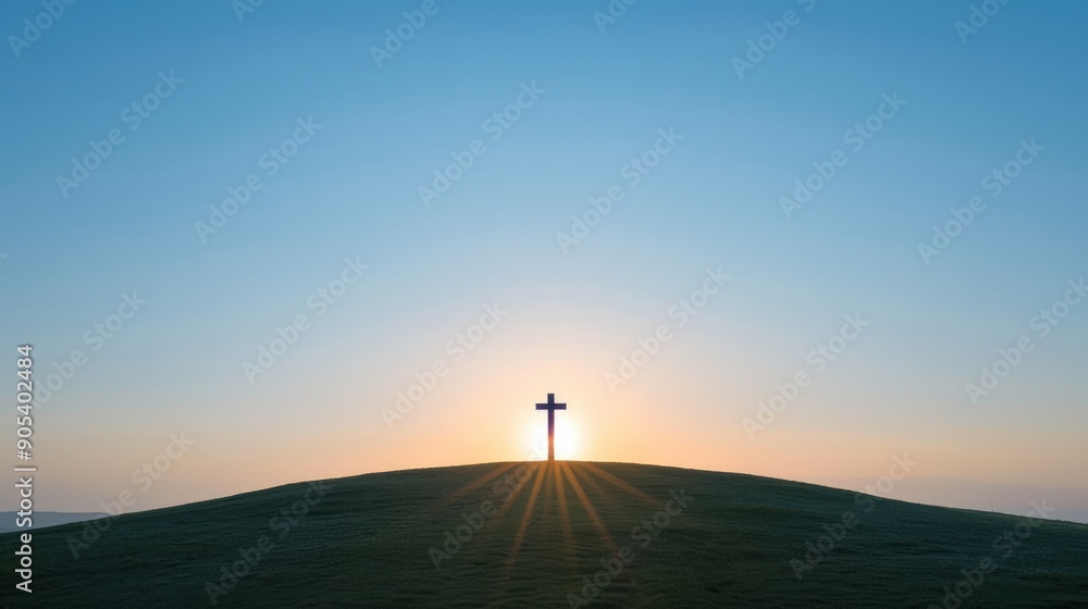 Obraz premium Silhouette of a cross on a hilltop with the sun rising behind it. The sky is a clear blue, and the ground is covered in grass.