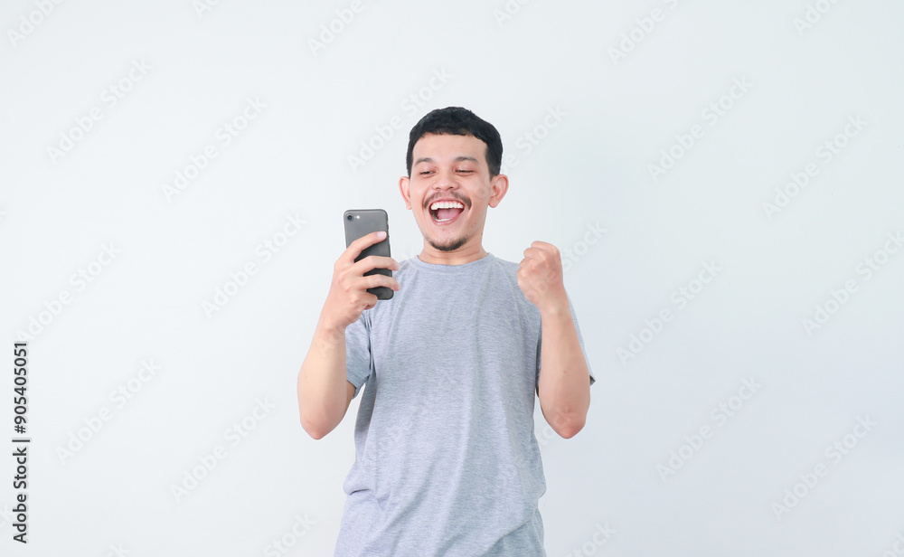 A man clenched fist and showing amazed facial expression when looking to handphone that he hold A man clenched fist and showing amazed facial expression when looking to handphone that he hold