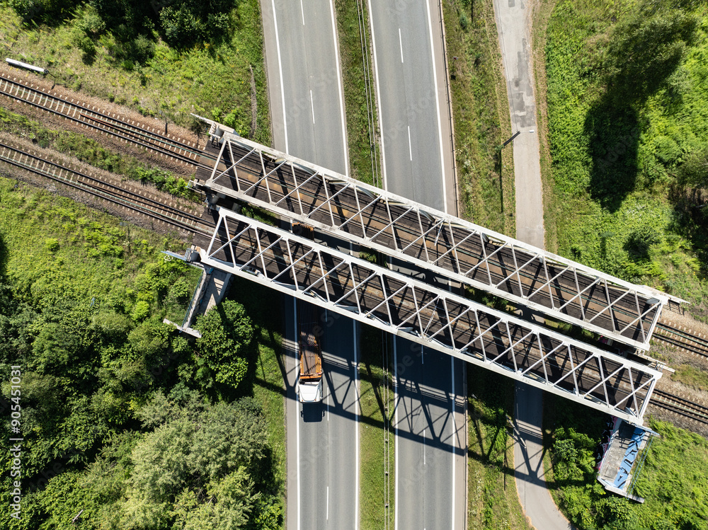 Fototapeta premium Aerial view from the drone of the railway bridge over the expressway. Freight train on metal iron bridge. Tracks and an iron railway bridge against the background of green fields.
