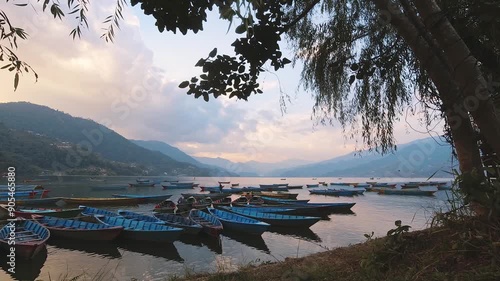 Time lapse stunning Phewa lake purple orange sunset panorama with traditional boats by shore. Travel sightseeing landmark in Nepal. Phewa Tal or Fewa lake. photo