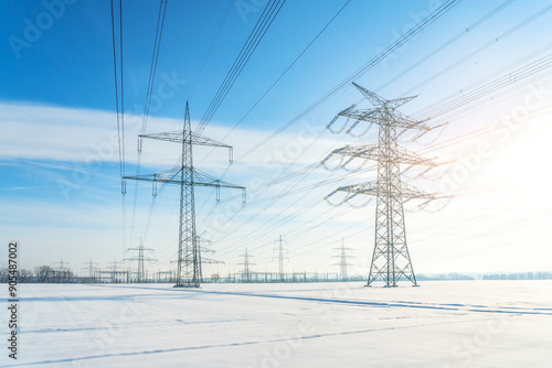 A lot of high voltage power line on the snowy field. Electrical energy transmission tower overhead line masts deep snow in winter. High voltage pylons, power pylons on the field in winter scenery