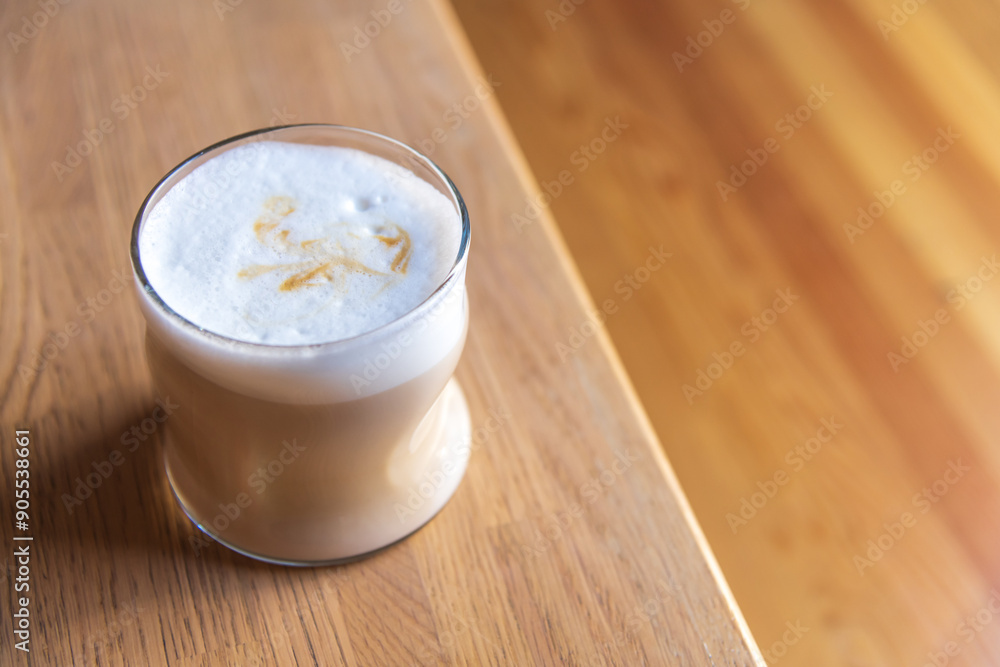 Close-up side view of drinking glass with latte macchiato standing on wooden table in cafe or restaurant. Copy space. Soft focus. Coffee beverages theme. Close-up side view of drinking glass with latte macchiato standing on wooden table in cafe or restaurant. Copy space. Soft focus. Coffee beverages theme.