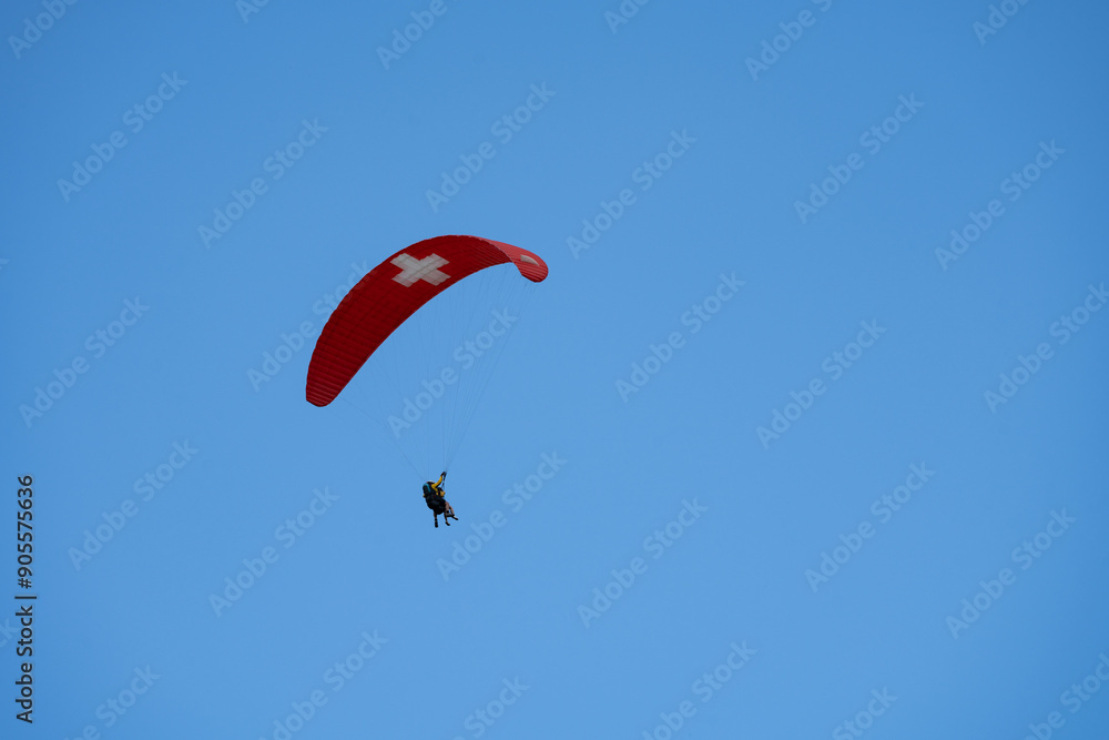 Tandem paragliders against a blue sky near Murren Switzerland in the Bernese Oberland, parachute with the Swiss flag Tandem paragliders against a blue sky near Murren Switzerland in the Bernese Oberland, parachute with the Swiss flag