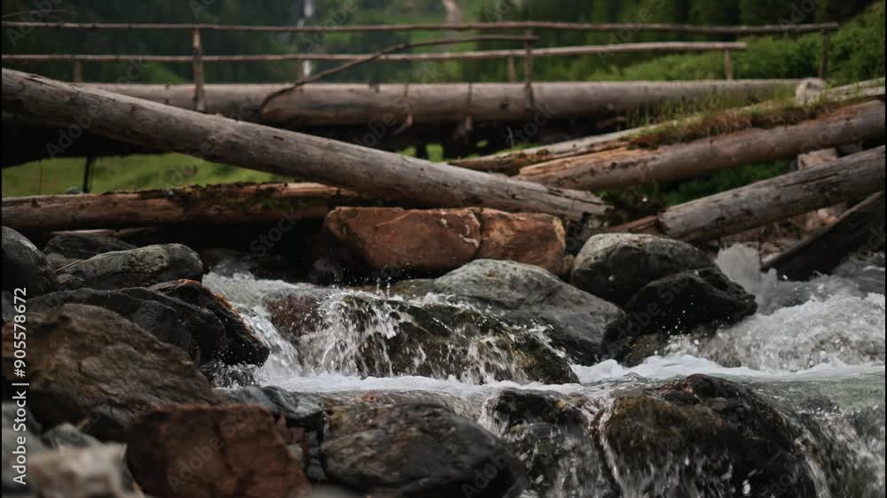 Slow motion close-up of water flowing over rocks on a wooden mountain bridge near a river, with a view of a mountain waterfall. Concept of hiking and a healthy lifestyle Slow motion close-up of water flowing over rocks on a wooden mountain bridge near a river, with a view of a mountain waterfall. Concept of hiking and a healthy lifestyle