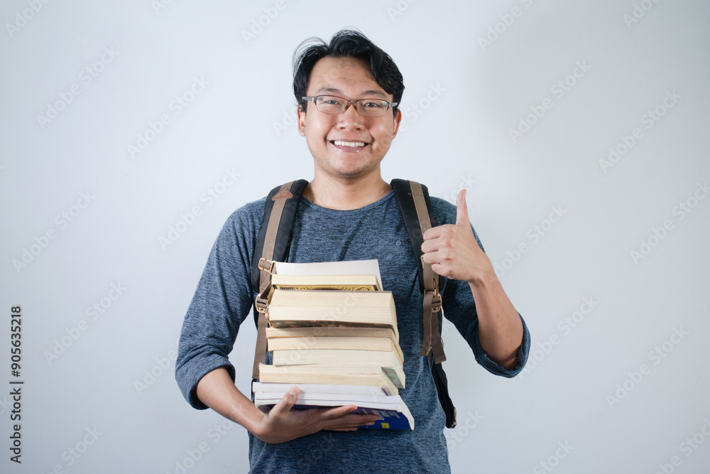 Asian young male student wearing bag and holding book smiling and happy expression. Ok hand sign gesture with isolated white background Asian young male student wearing bag and holding book smiling and happy expression. Ok hand sign gesture with isolated white background