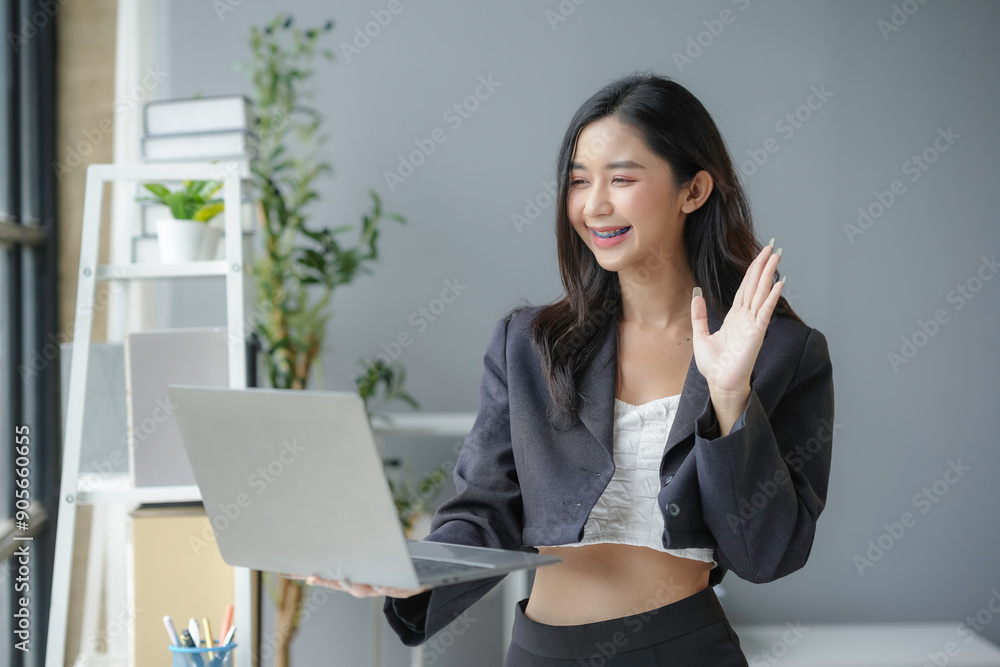 Smiling young asian businesswoman holding laptop and waving during video call in modern office Smiling young asian businesswoman holding laptop and waving during video call in modern office