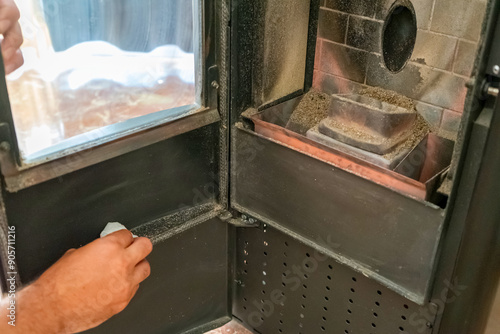 Close-up of a man cleaning the soot produced by the pellet stove in his living room, sustainable heat. Renewable energy.