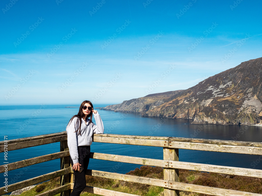 Young teenager girl exploring beautiful Sliabh Liag, county Donegal, Ireland. Travel and tourism. Warm sunny day. Stunning Irish nature landscape scene in the background.