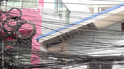 A tangled mess of wires and cables hanging from a building. The wires are black and appear to be in disarray