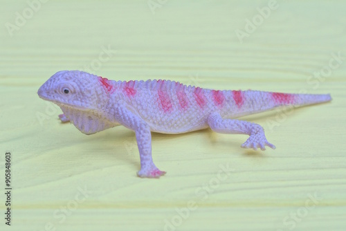 one plastic gray red toy lizard lies on yellow wooden table photo