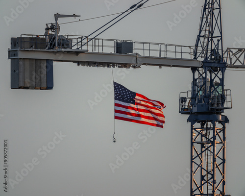 United States flag gracefully flying, back lit by setting sun and hanging from crane on a construction site.