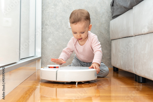 A baby slaps his palm on the surface of a robot vacuum cleaner. Concept of learning about surrounding objects