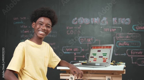 Smart african boy use laptop to code program and turn around to wave hand. Cute high school stident coding engineering prompt or program system at blackboard in STEM technology classroom. Edification photo