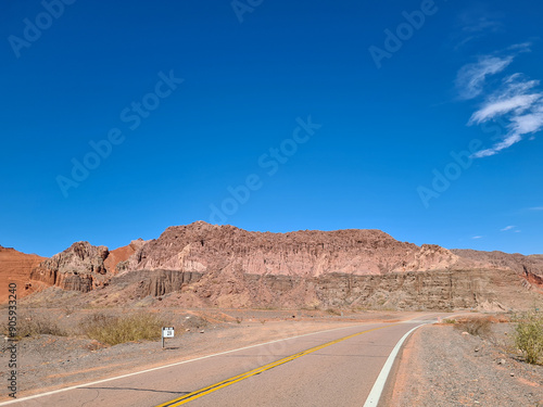 Paved highway in the desert with mountains of sedimentary rocks in the background