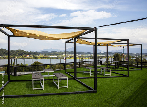 Chungju-si, Chungcheongbuk-do, South Korea - September 23, 2022: Summer view of table and chair with artificial turf and shade on rooftop of a building against Chungjuho Lake and Namhan River
 photo