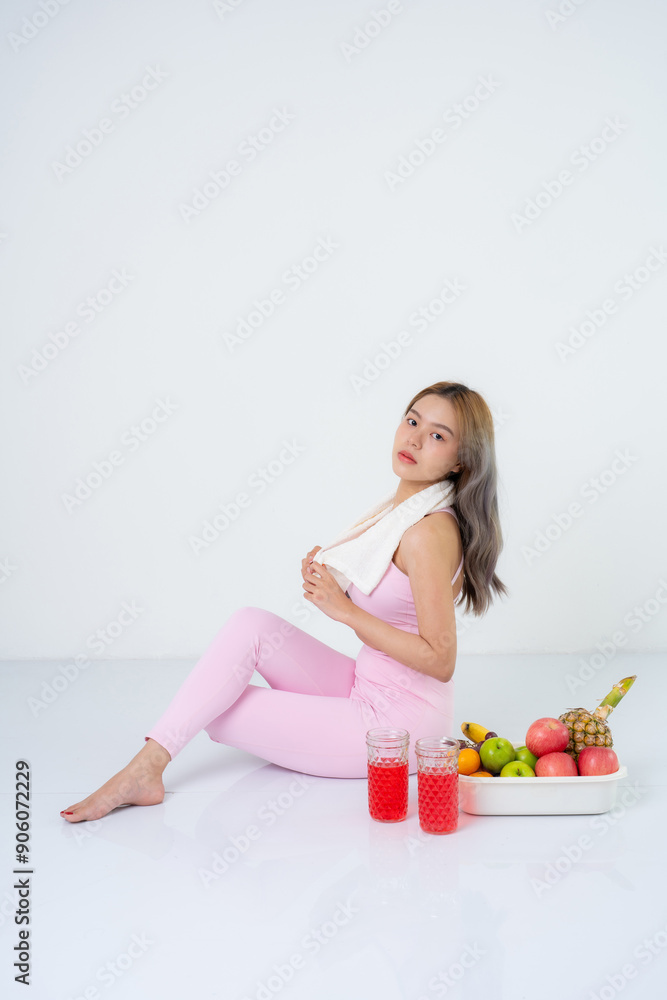 Healthy Asian woman with long hair wearing a pink sportswear, drinking a sports drink and having various fruits. She is photographed in a studio and is a gym fitness presenter. Healthy Asian woman with long hair wearing a pink sportswear, drinking a sports drink and having various fruits. She is photographed in a studio and is a gym fitness presenter.