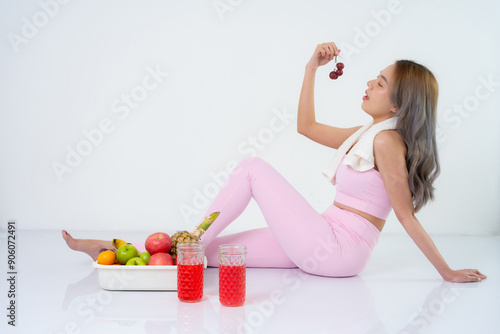 Asian female fitness model with long hair, holding grapes and eating fruits and electrolyte drink, taking pictures in the studio, wearing pink sportswear, good figure and good health as a presenter.