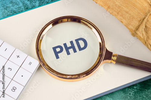 The word PHD is written appeared through a magnifying glass in a notebook, close-up. View from above