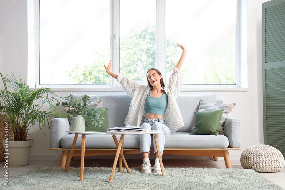 Young woman stretching on grey sofa in living room Young woman stretching on grey sofa in living room