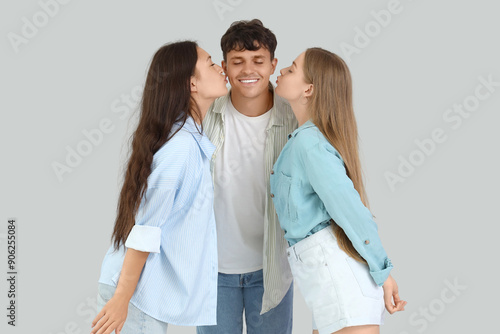 Young man with two women kissing on light background. Polyamory concept photo