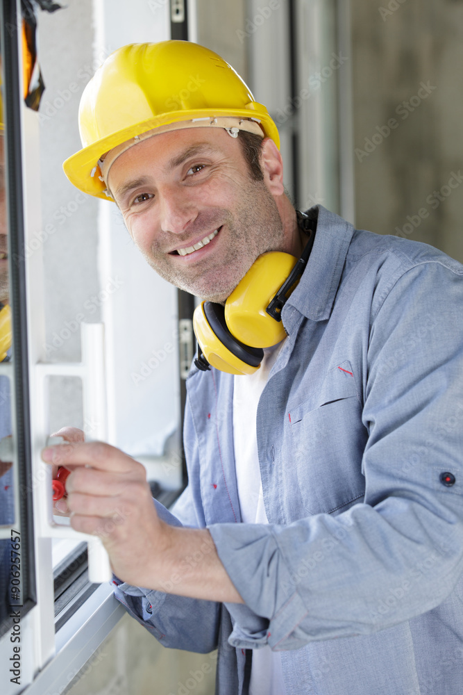 happy builder standing with drill infront of window happy builder standing with drill infront of window