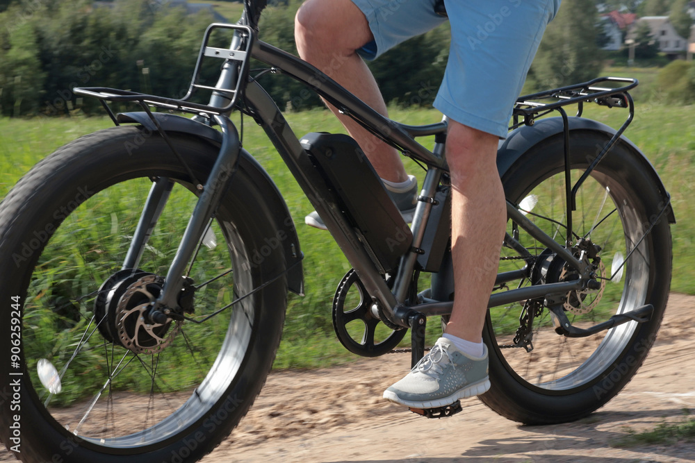 Cyclist on electric bicycle riding along path in field in countryside at sunset close-up. Sport and health. Summer hobby. Cyclist on electric bicycle riding along path in field in countryside at sunset close-up. Sport and health. Summer hobby.